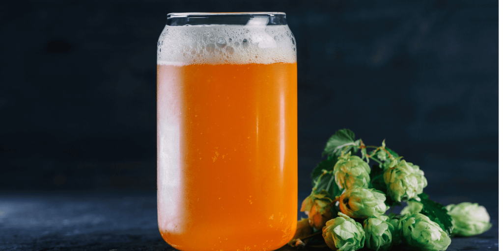 hazy ipa in a glass with hops beside it
