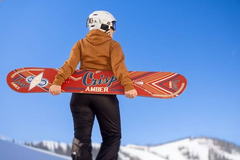 Woman in the outdoors carrying a Crisp Amber x Gilson snowboard