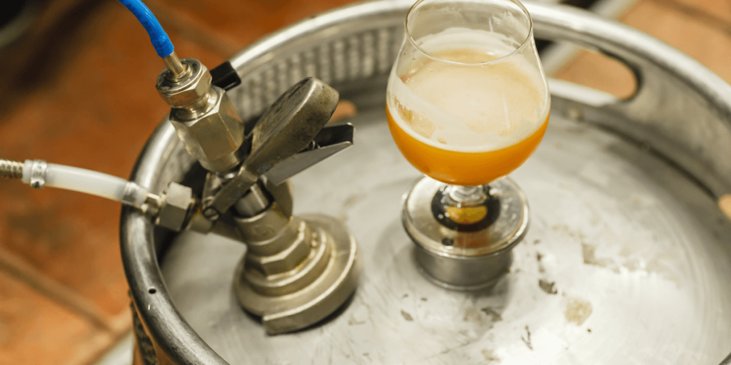 glass of beer on top of a metal beer keg